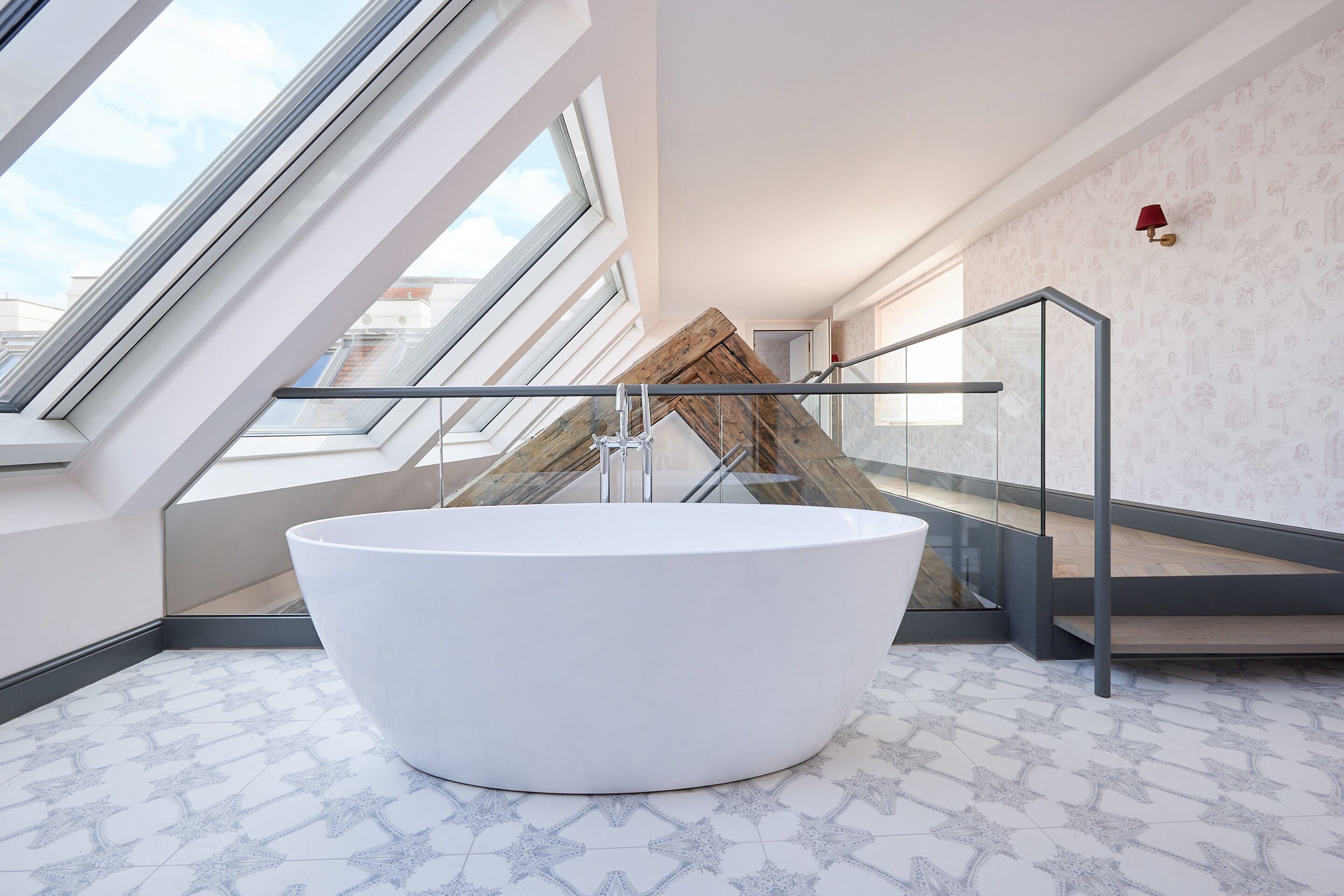 Un baño moderno con una bañera independiente, tragaluces y una escalera que conduce a un nivel superior.