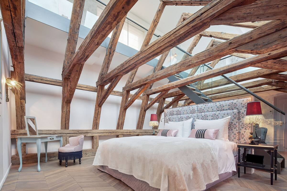Un dormitorio con una cama grande, vigas de madera, una silla y una mesa.