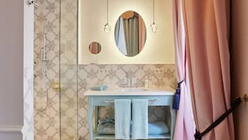 Un baño con ducha, lavabo y espejo. Hay toallas colgadas en un perchero y una cortina parcialmente abierta.