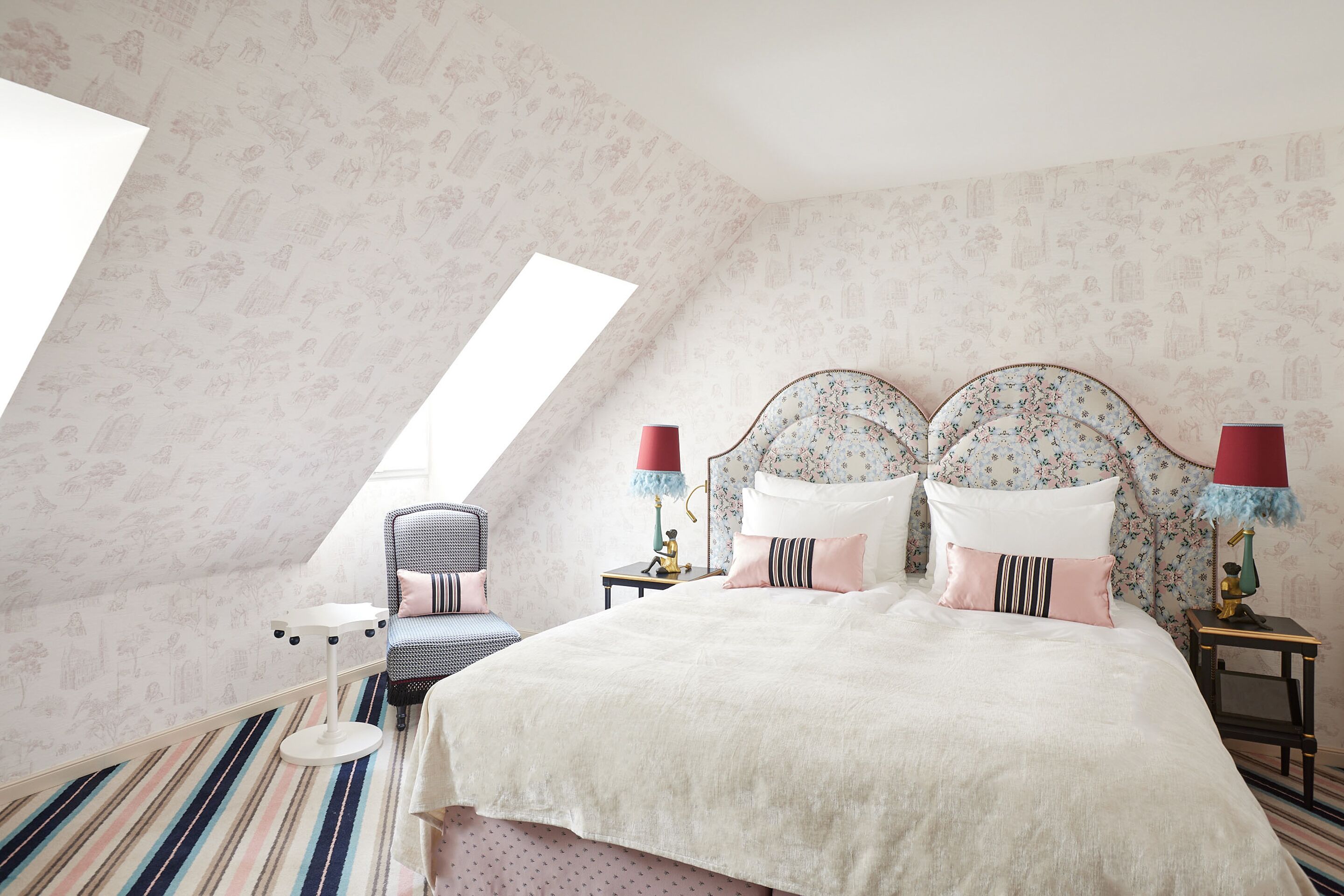Une chambre avec un plafond en pente, un lit doté d’une tête de lit à motifs floraux, des coussins à rayures et un tapis à rayures.