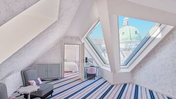 A modern loft bedroom with a sloped ceiling, a large skylight, a striped carpet, a bed, a desk, and a view of a dome building.