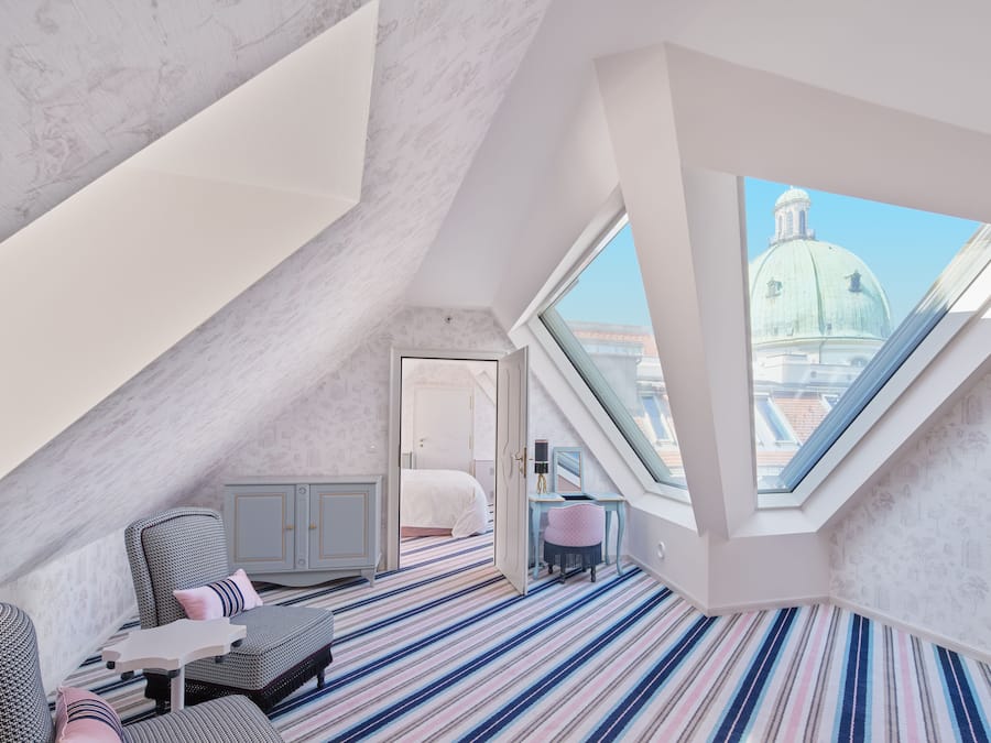 A modern loft bedroom with a sloped ceiling, a large skylight, a striped carpet, a bed, a desk, and a view of a dome building.
