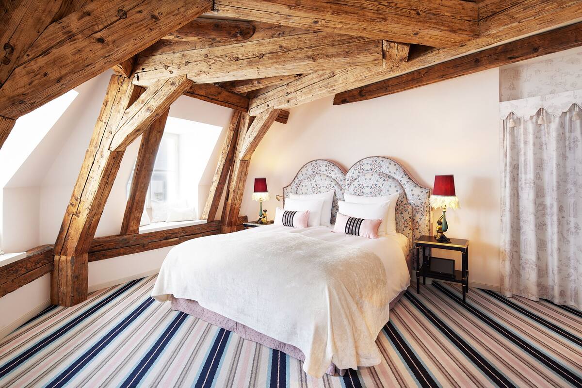 Un dormitorio con techo inclinado, una cama grande con dos mesitas de noche y un suelo a rayas.