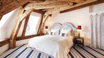 Une chambre avec un plafond en pente, un grand lit avec deux tables de chevet et un sol à rayures.