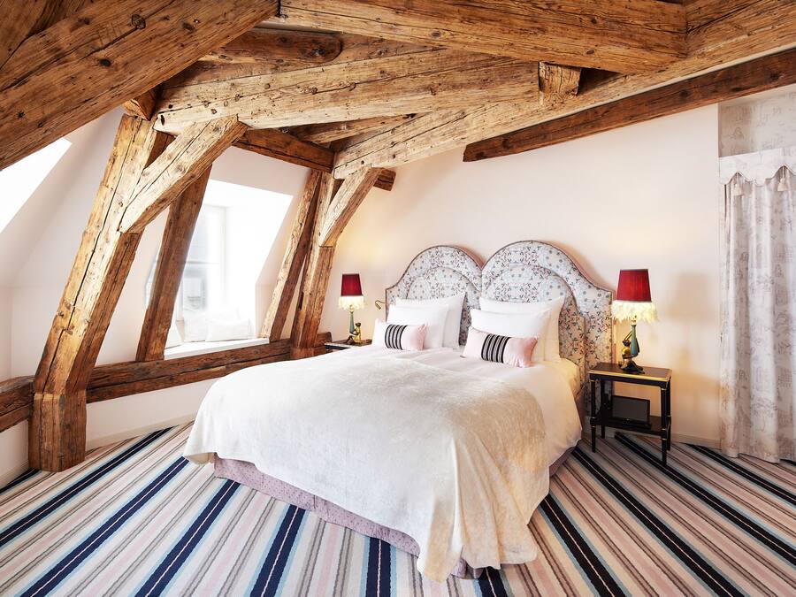 Une chambre avec un plafond en pente, un grand lit avec deux tables de chevet et un sol à rayures.