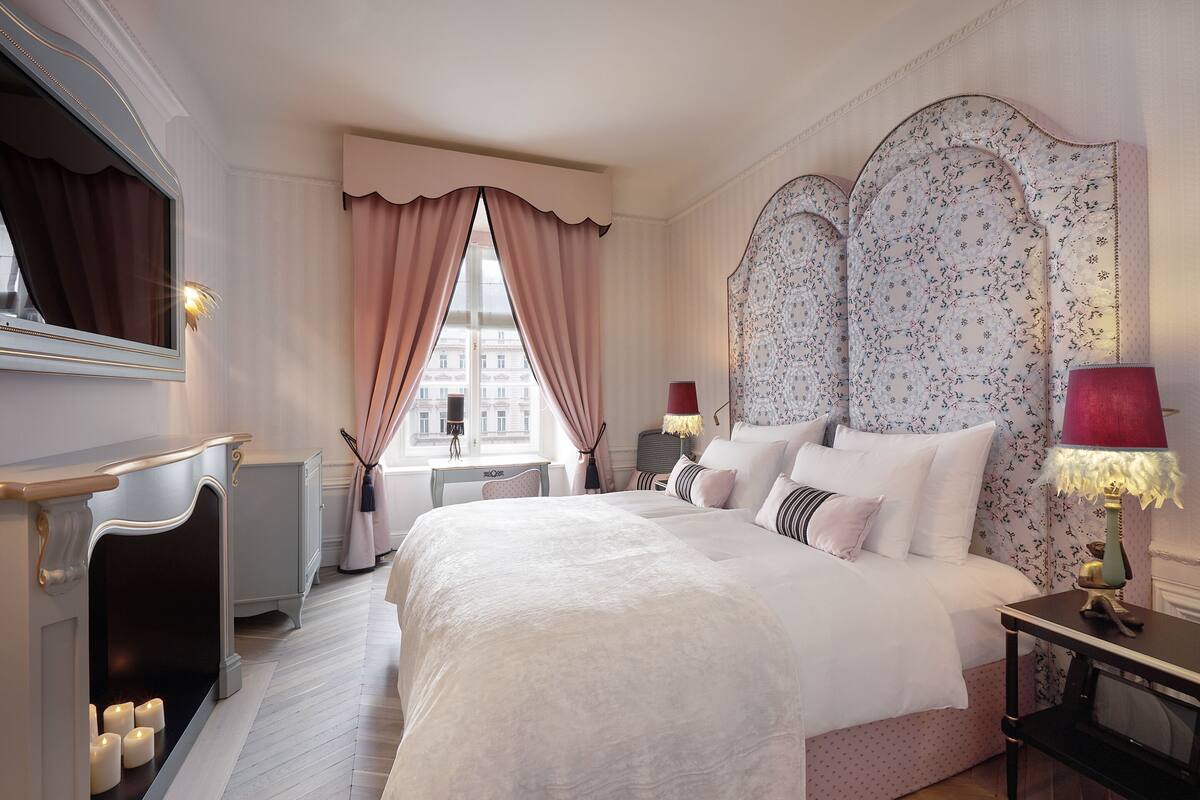 Habitación de hotel con una cama grande, chimenea, escritorio y vistas a edificios fuera de la ventana.