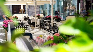 An outdoor dining area with tables set for two, surrounded by greenery and flowers. - The Leo Grand (Vienna)