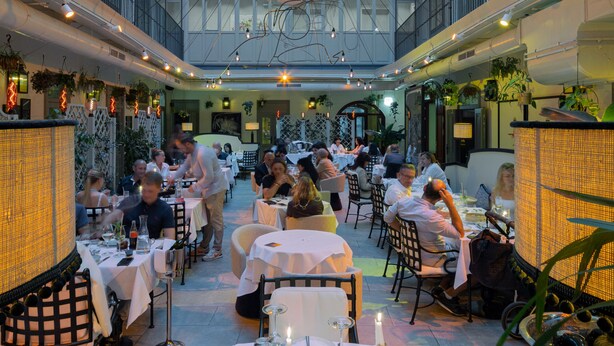 A spacious indoor dining area with high ceilings and multiple dining tables, surrounded by balconies and a central decorative element. - The Leo Grand (Vienna)