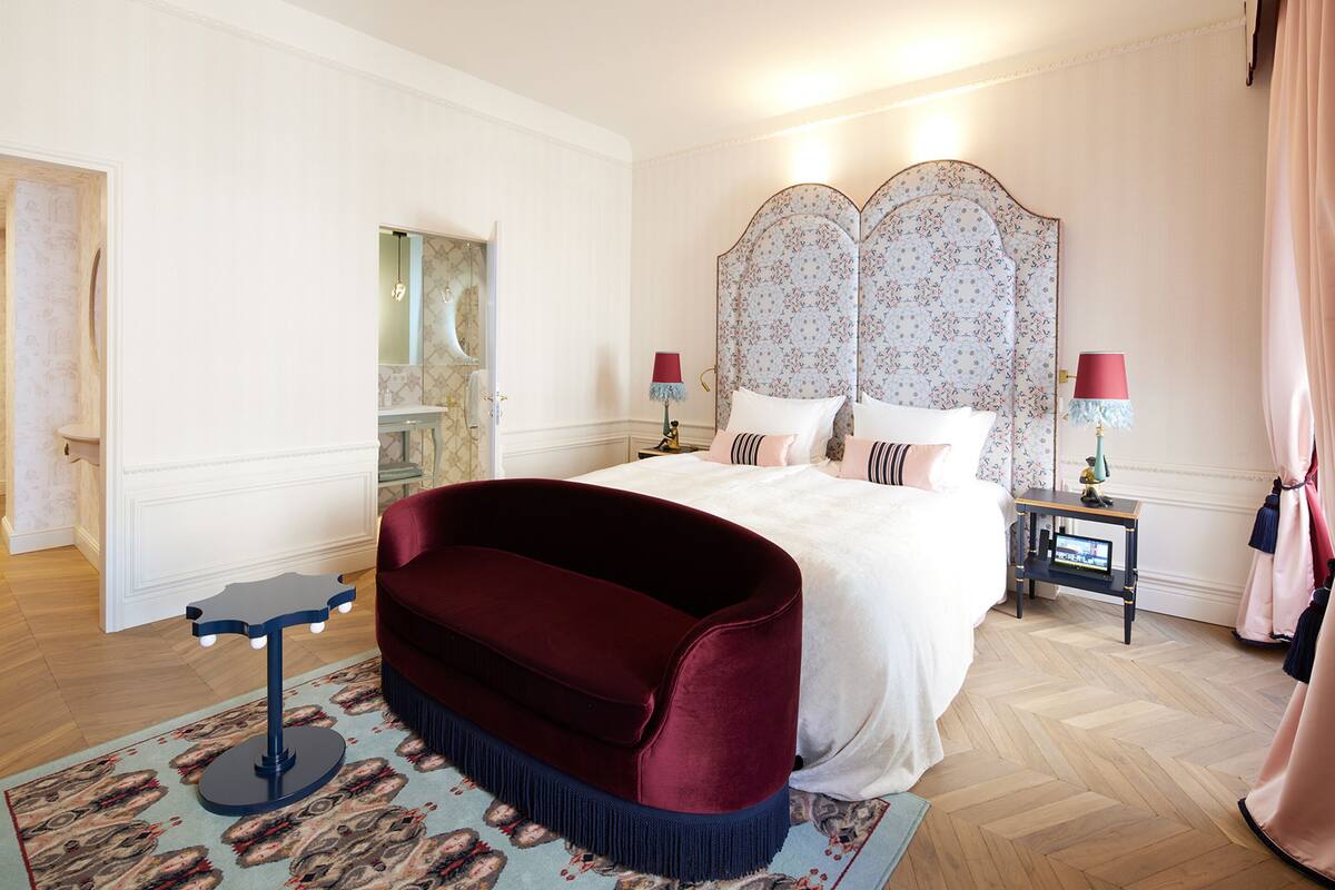 Un dormitorio con una cama grande, un sofá de terciopelo rojo, una mesita de noche con lámpara y un espejo.