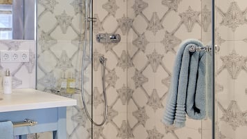 Ein Badezimmer mit gemusterten Fliesen, einer Duschkabine aus Glas, einem Handtuchhalter mit Handtüchern, einem Waschbecken mit Toilettenartikeln und einem Spiegel.