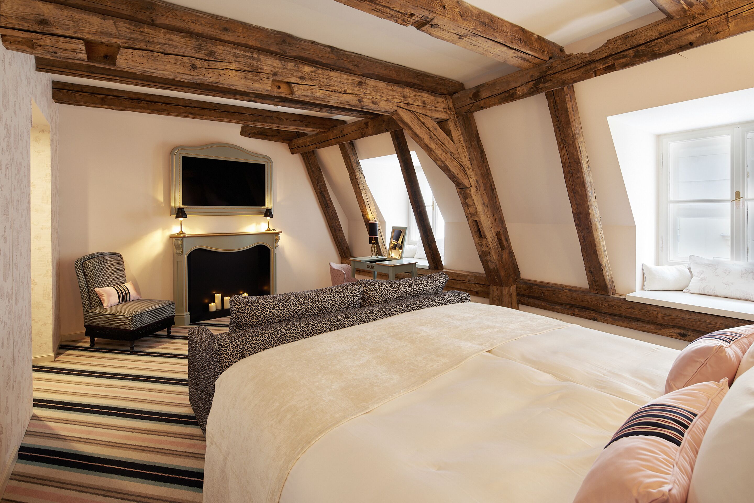 A bedroom with a large bed, a chair, a fireplace, and a window.