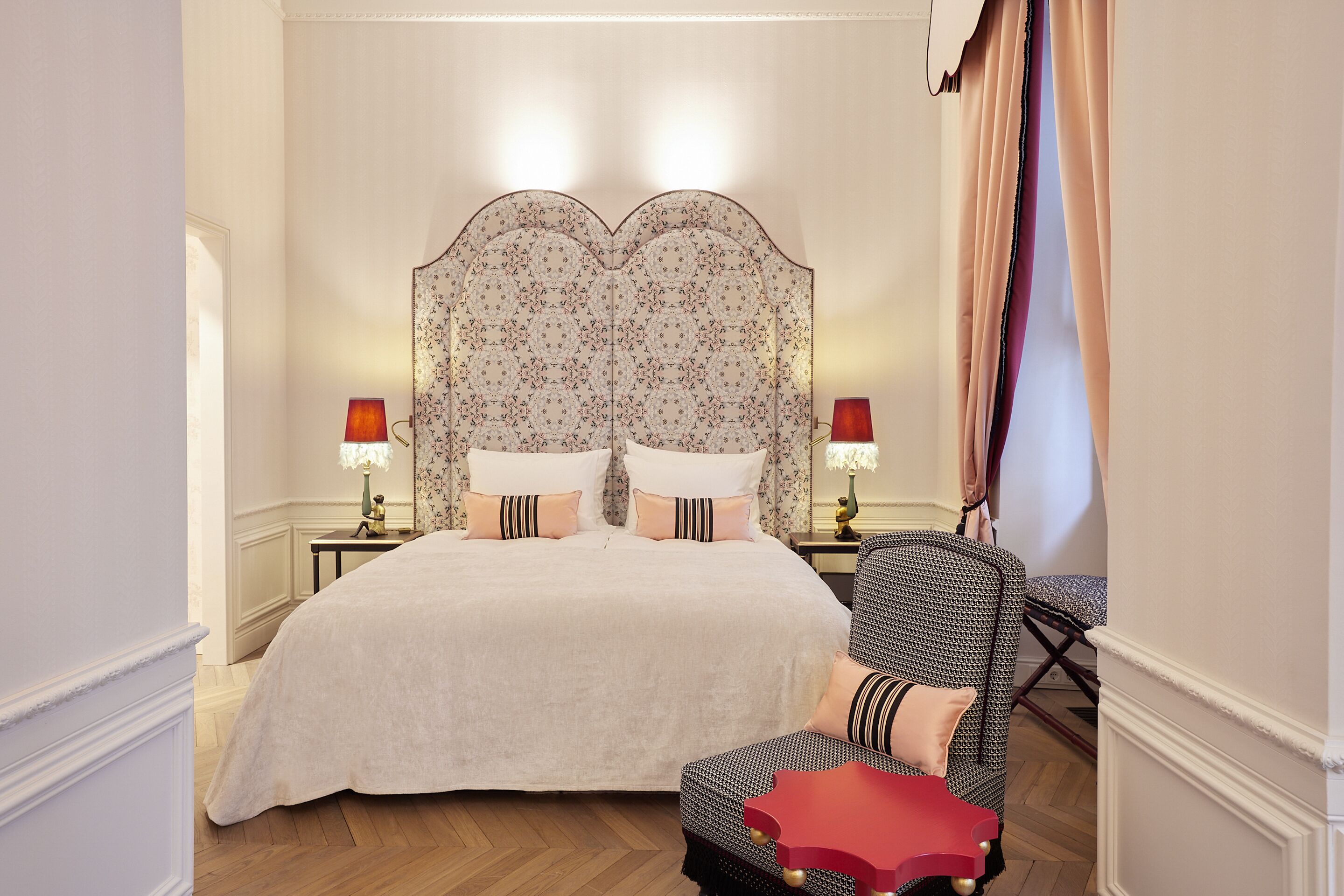 Un dormitorio con una cama grande, dos mesitas de noche con lámparas, una silla y un cabecero decorativo.