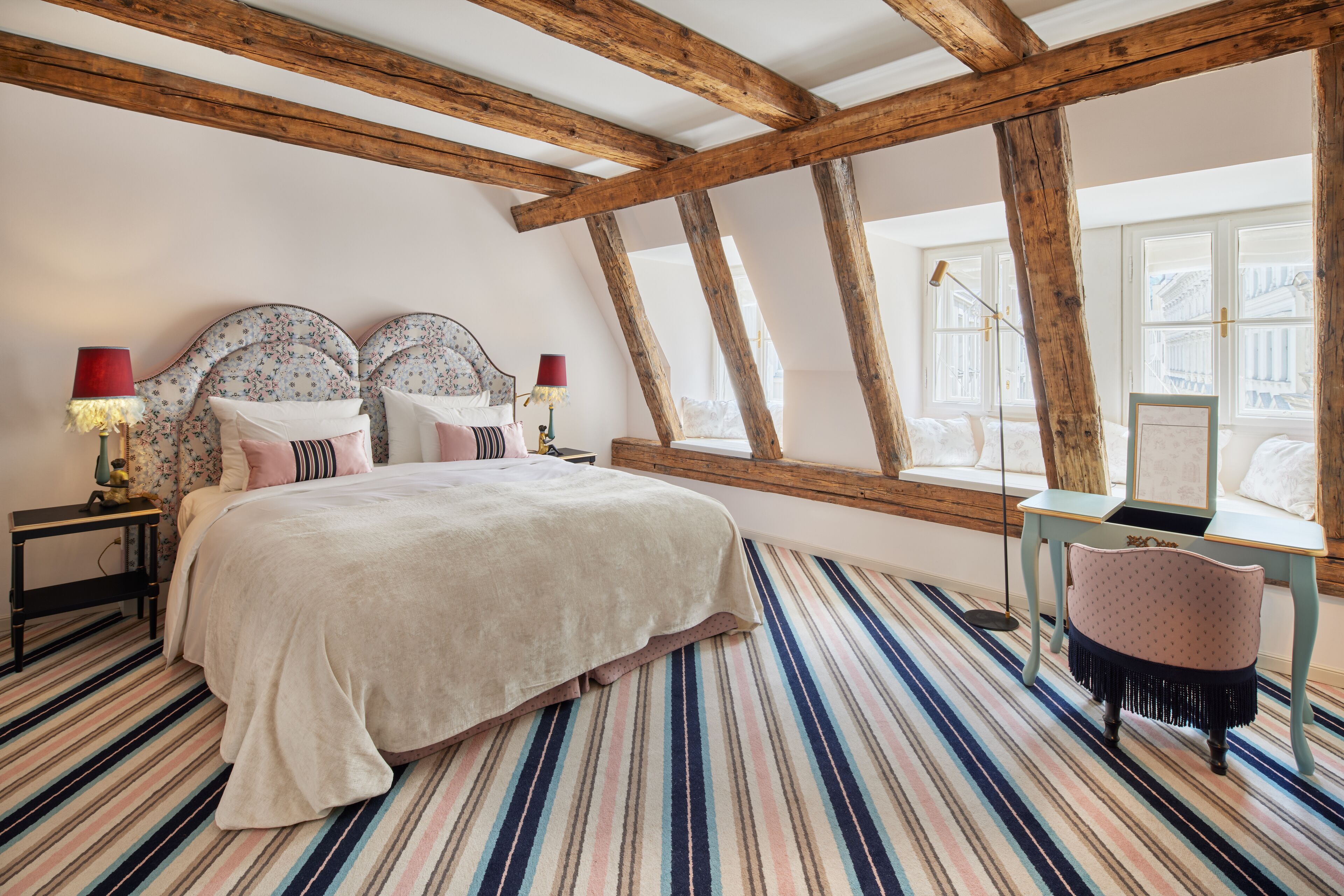 Un dormitorio con una cama grande, vigas de madera, un suelo de alfombra a rayas y una ventana con vistas.