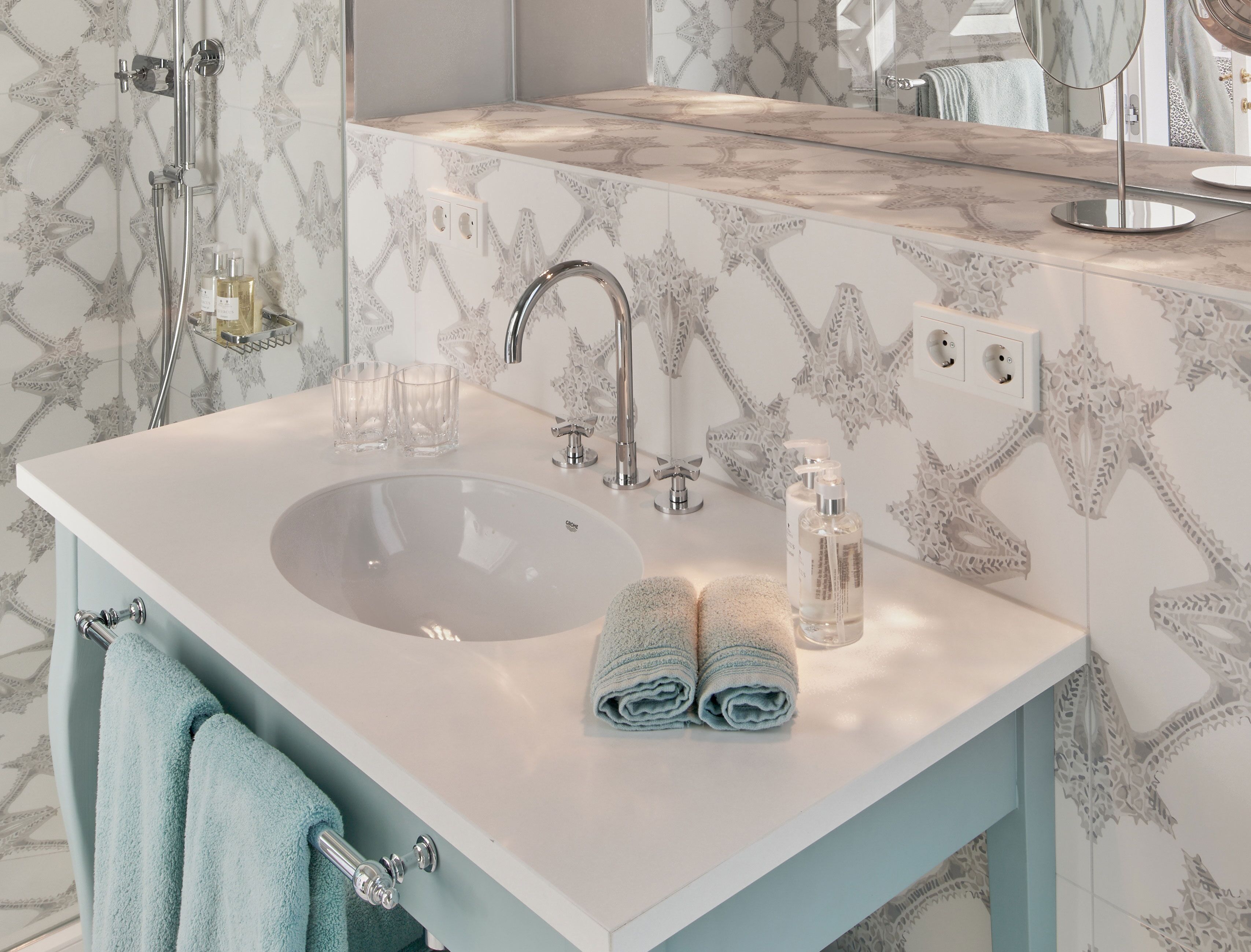 A bathroom with a white sink, two clear glasses, a towel, and a bottle of liquid soap.