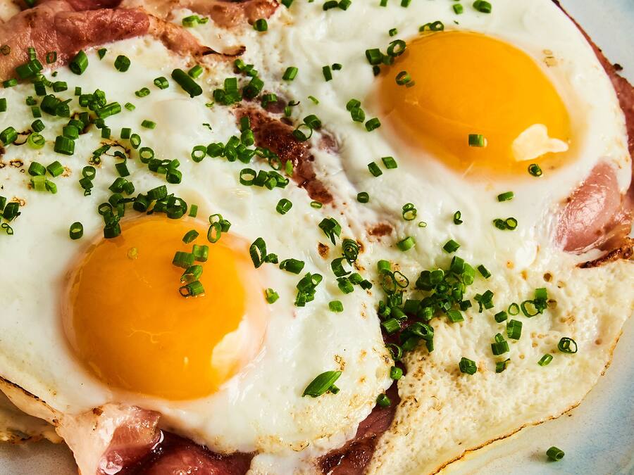 A close-up of two fried eggs with green onions on top.
