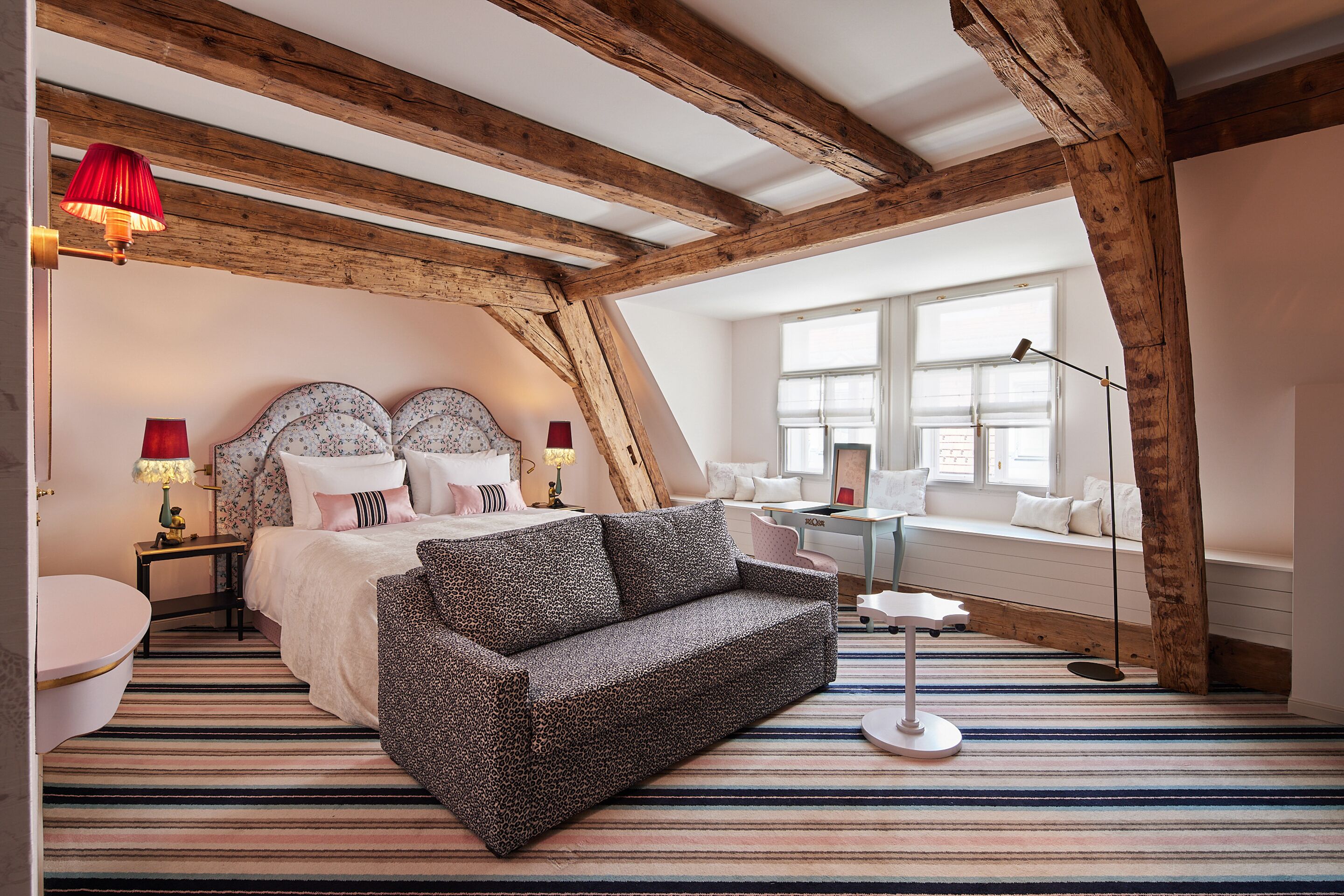 Un dormitorio con cama, sofá, mesita de noche, lámpara, ventana y vistas al exterior.