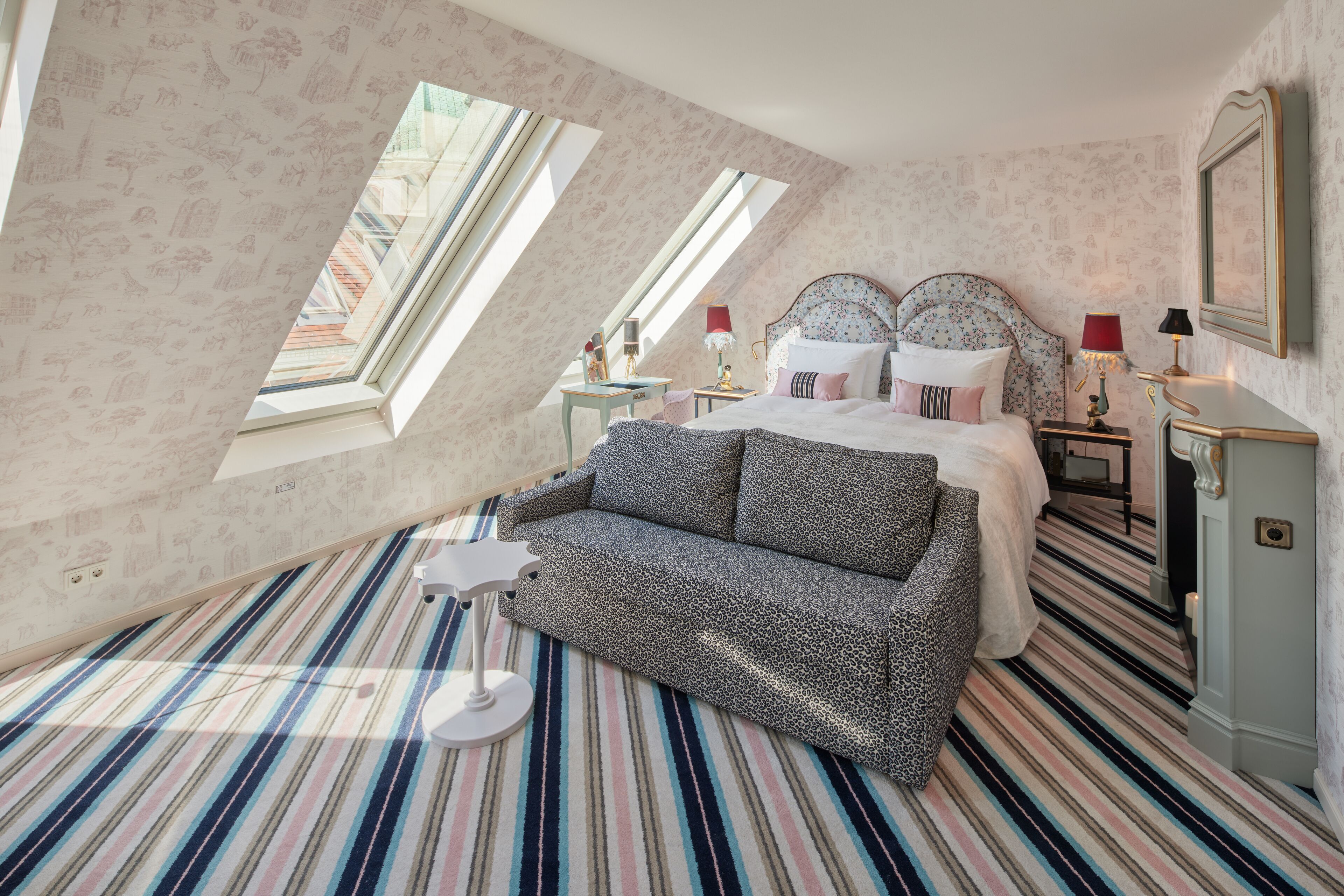 A bedroom with a sloped ceiling, a bed with a floral headboard, a striped floor, and a small table with a lamp.