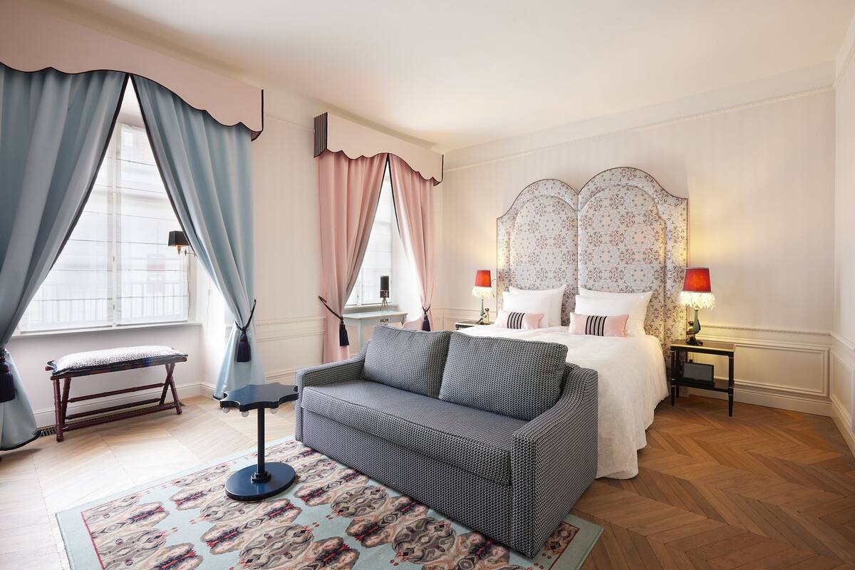 Un dormitorio con una cama, un sofá, un banco y una mesita de noche con lámparas.