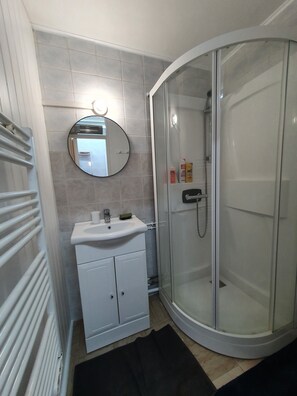 Features a glass-enclosed shower, round mirror, and radiator for comfort.