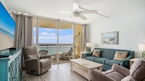 A spacious living area with a balcony, a ceiling fan, a sofa, a coffee table, and a TV.