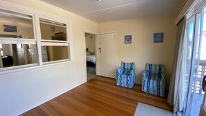 Un couloir avec un plancher en bois, un lit dans la pièce adjacente et deux fauteuils à rayures.