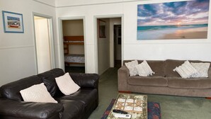 Un salon avec un canapé en cuir marron, un divan marron et une table basse sur laquelle est posé un jeu de société. Un tableau représentant une scène de plage est accroché au mur.
