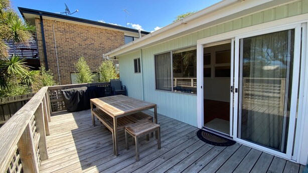 Une terrasse dotée d’une table et de chaises en bois, d’un barbecue et d’une porte-fenêtre coulissante donnant sur un patio abrité.