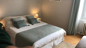 Una camera da letto con un letto, cuscini, una lampada da comodino, un quadro appeso e una finestra con tende.