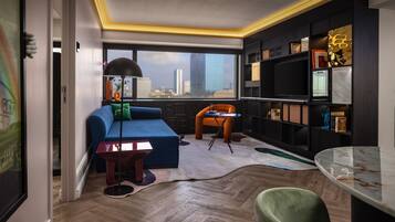 A modern living room with a blue sofa, orange chair, and a city view through large windows.