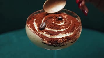 A dessert with a spoon on top, placed on a teal surface.