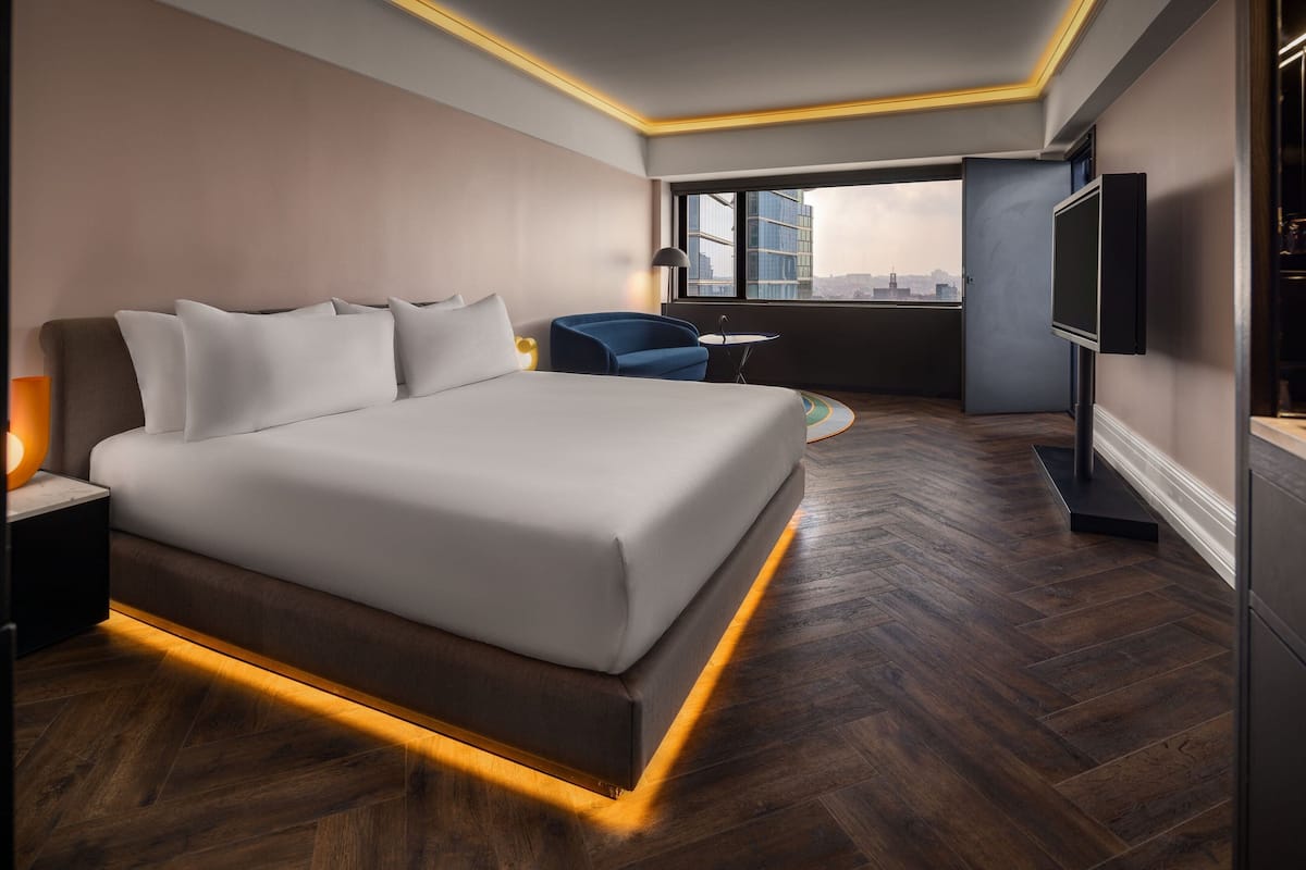 Ein modernes Hotelzimmer mit einem großen Bett, einem Schreibtisch, einem Sessel und einem Fernseher.