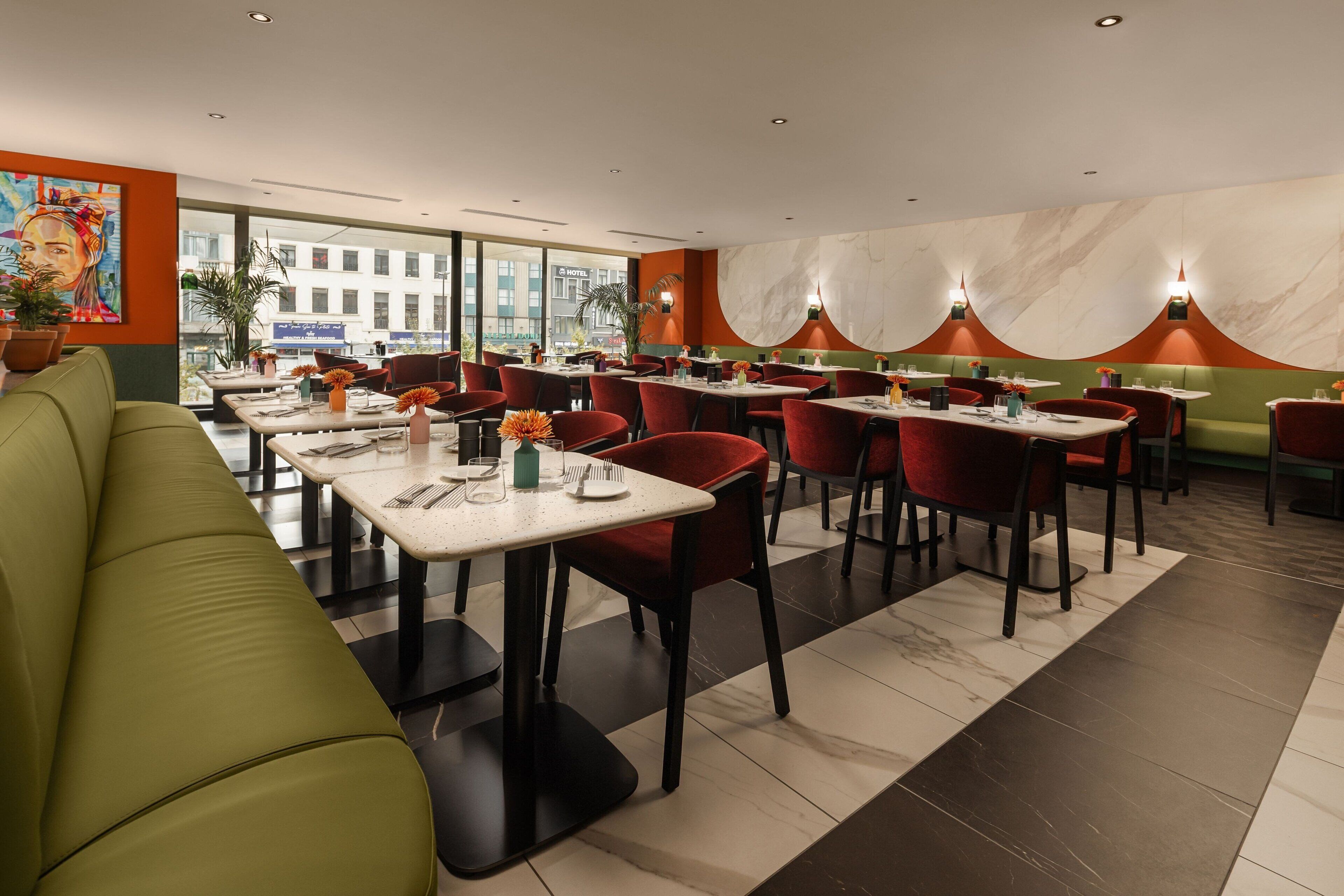 A restaurant with a green sofa, red chairs, and marble walls. Tables are set with plates, glasses, and cutlery.