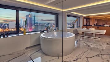 A modern bathroom with a large bathtub, a massage table, and a city view through large windows.