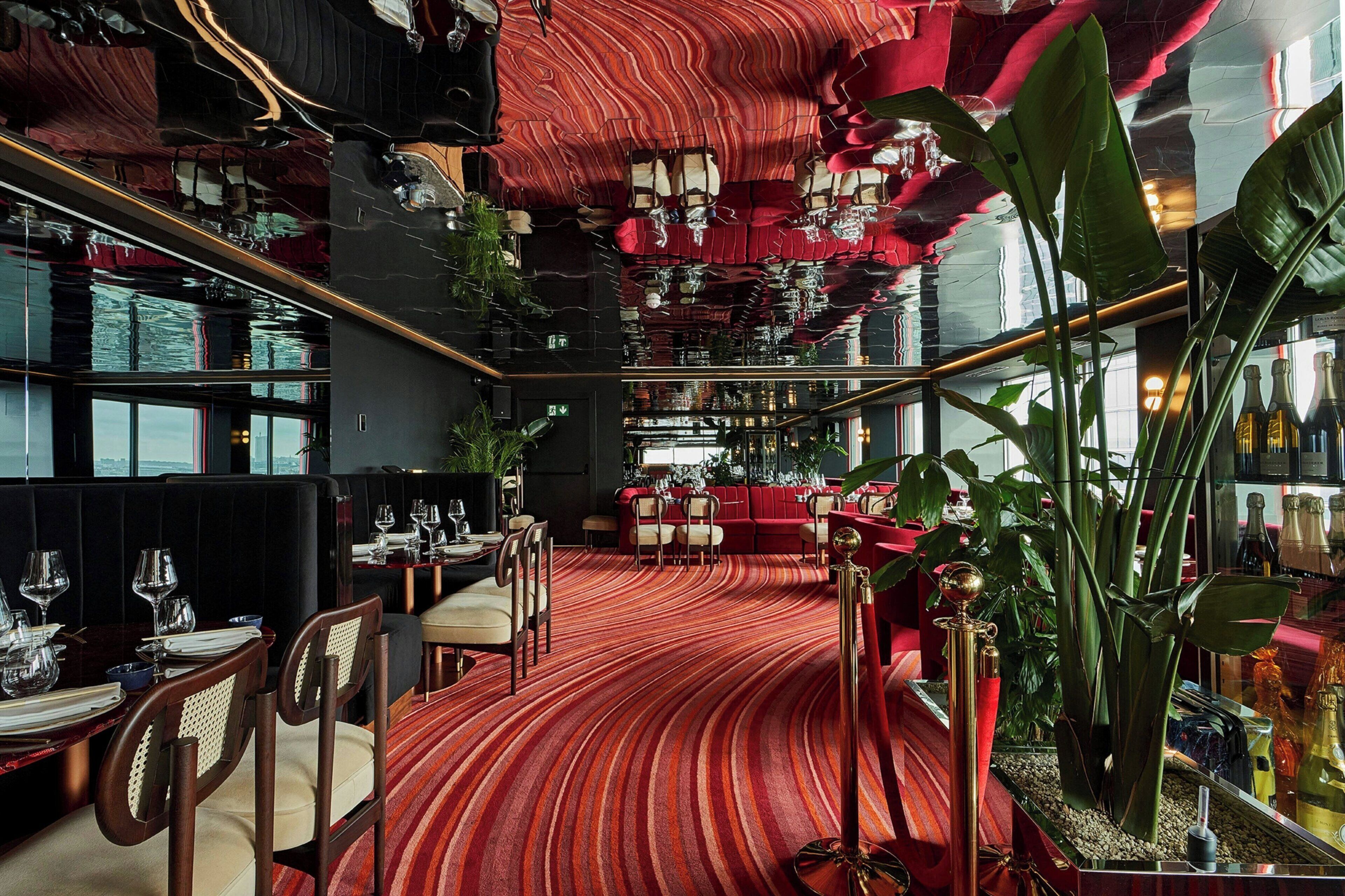 A restaurant with a red striped carpet, wooden furniture, and a modern ceiling design.