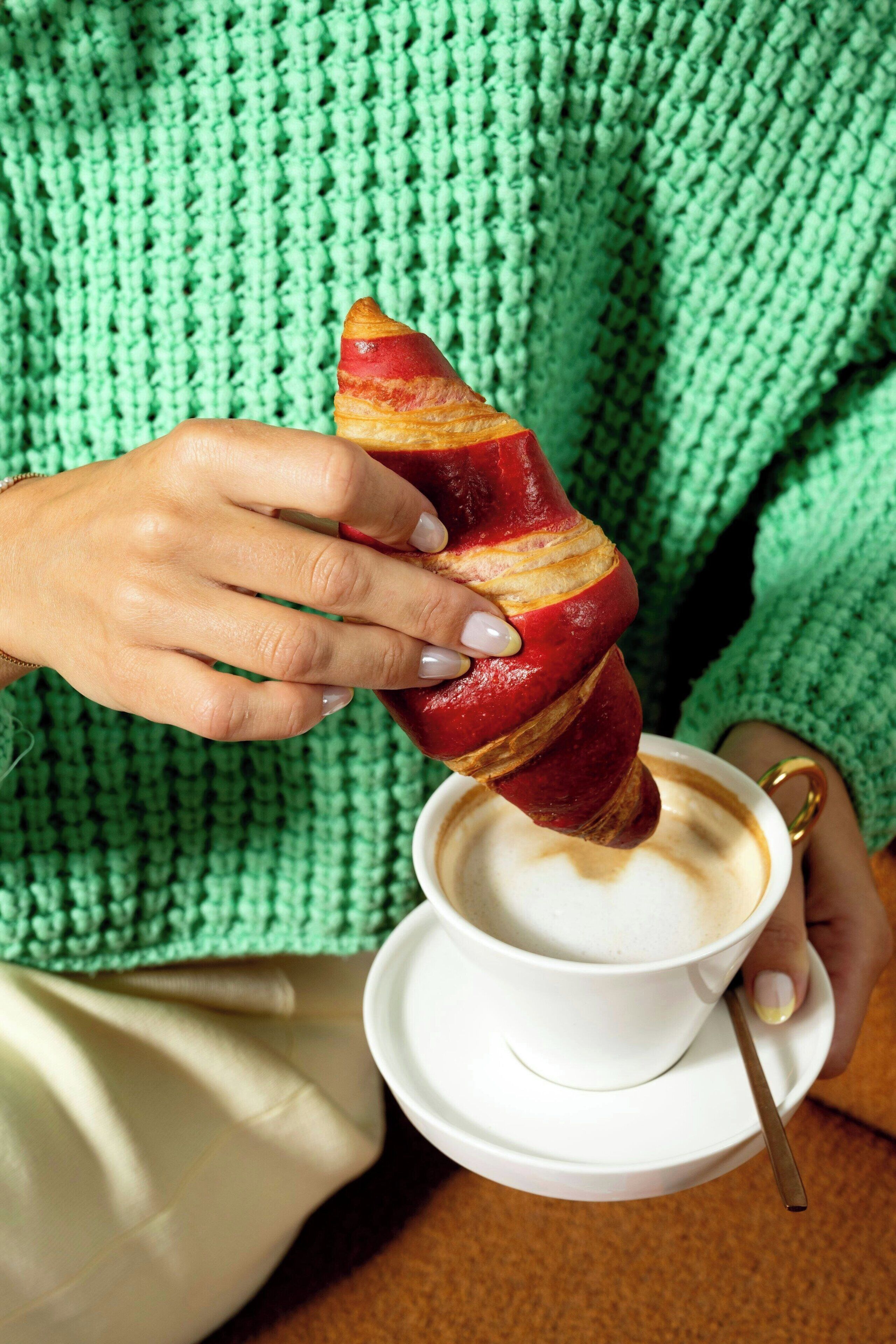Una persona sosteniendo un croissant sobre una taza de café.