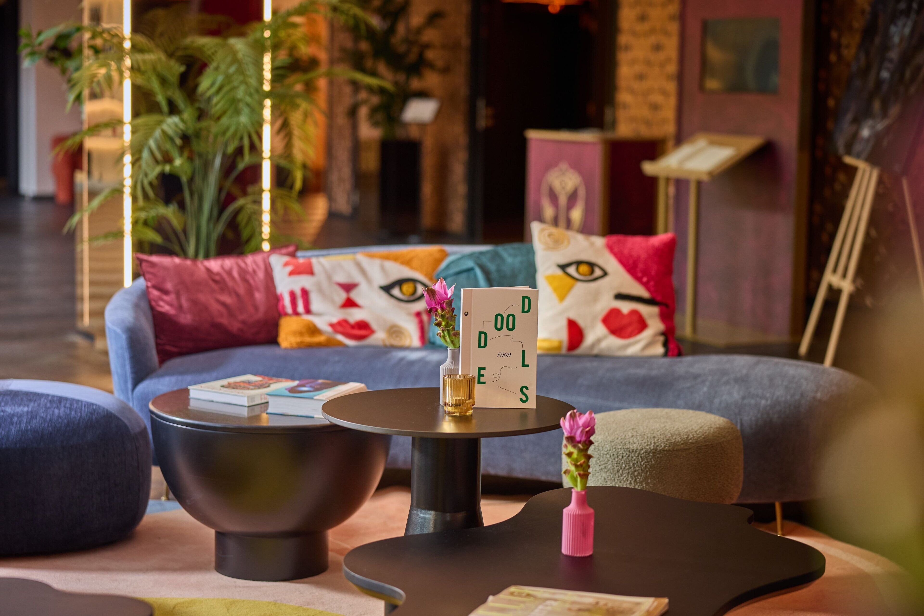 Un área lounge moderna con un sofá, una mesa redonda y un taburete pequeño. Hay un letrero con la palabra “DOOLS”.