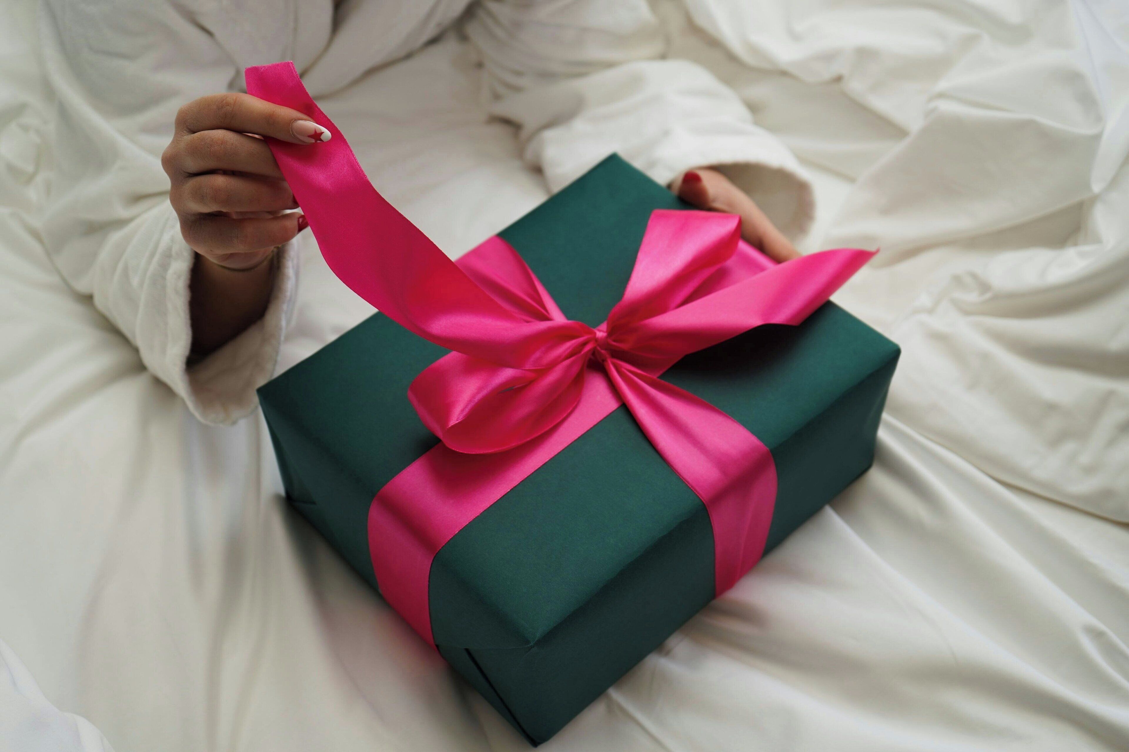 Une personne tenant une boîte cadeau verte avec un ruban rose.