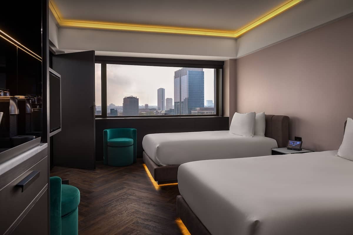 Ein modernes Hotelzimmer mit zwei Betten, einem Fernseher, einem Schreibtisch und Blick auf die Stadtlandschaft.
