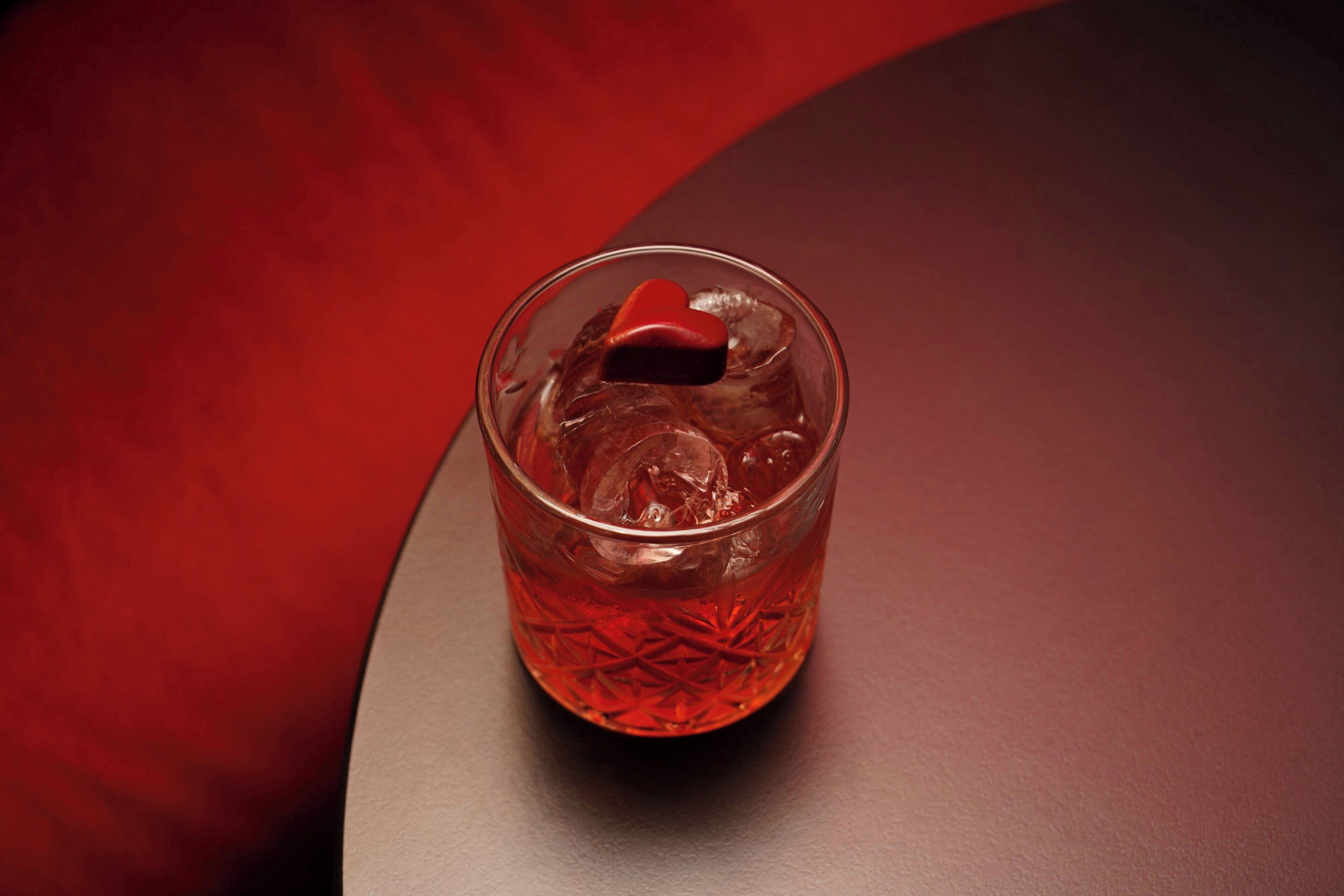 Een glas met een ijsblokje in de vorm van een hart op een donkere ondergrond.