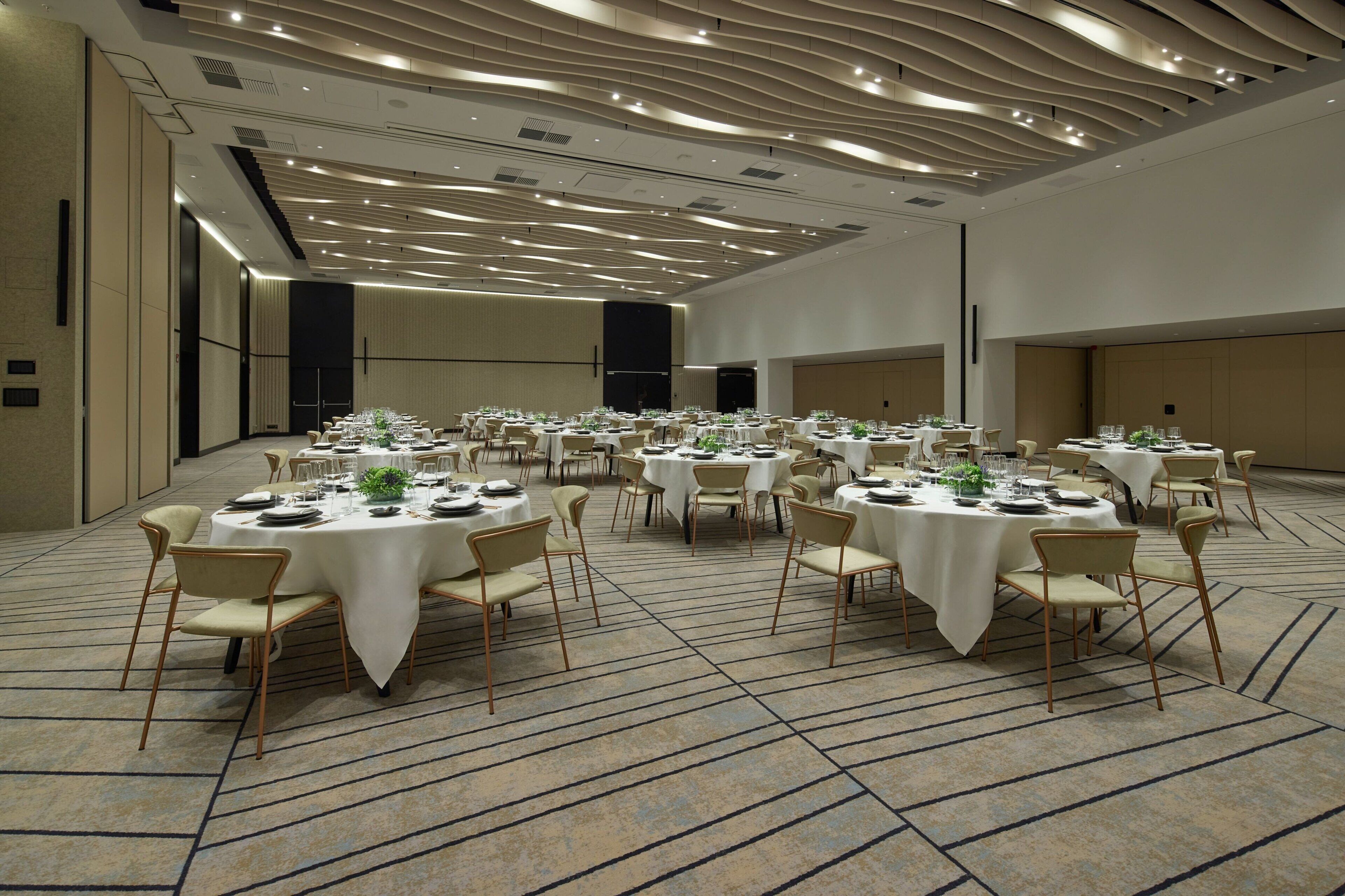 Un amplio salón de banquetes con mesas redondas dispuestas para comer, equipado con sillas y menaje de mesa.