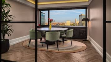 Uma sala de jantar moderna com uma mesa redonda e seis cadeiras, uma planta em vaso e vista para o horizonte da cidade através de grandes janelas.