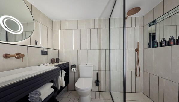 A modern bathroom with a white toilet, a black vanity with a mirror, and a shower area with a handheld showerhead. - Cardo Brussels, Autograph Collection (Brussels)