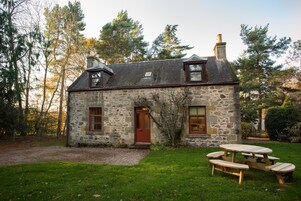 A stone house with a wooden door, a chimney, and a picnic table in the yard.