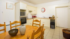 Una pequeña cocina con alacenas blancas, un microondas, un lavamanos y un reloj en la pared.