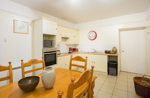 A small kitchen with white cabinets, a microwave, a sink, and a clock on the wall.