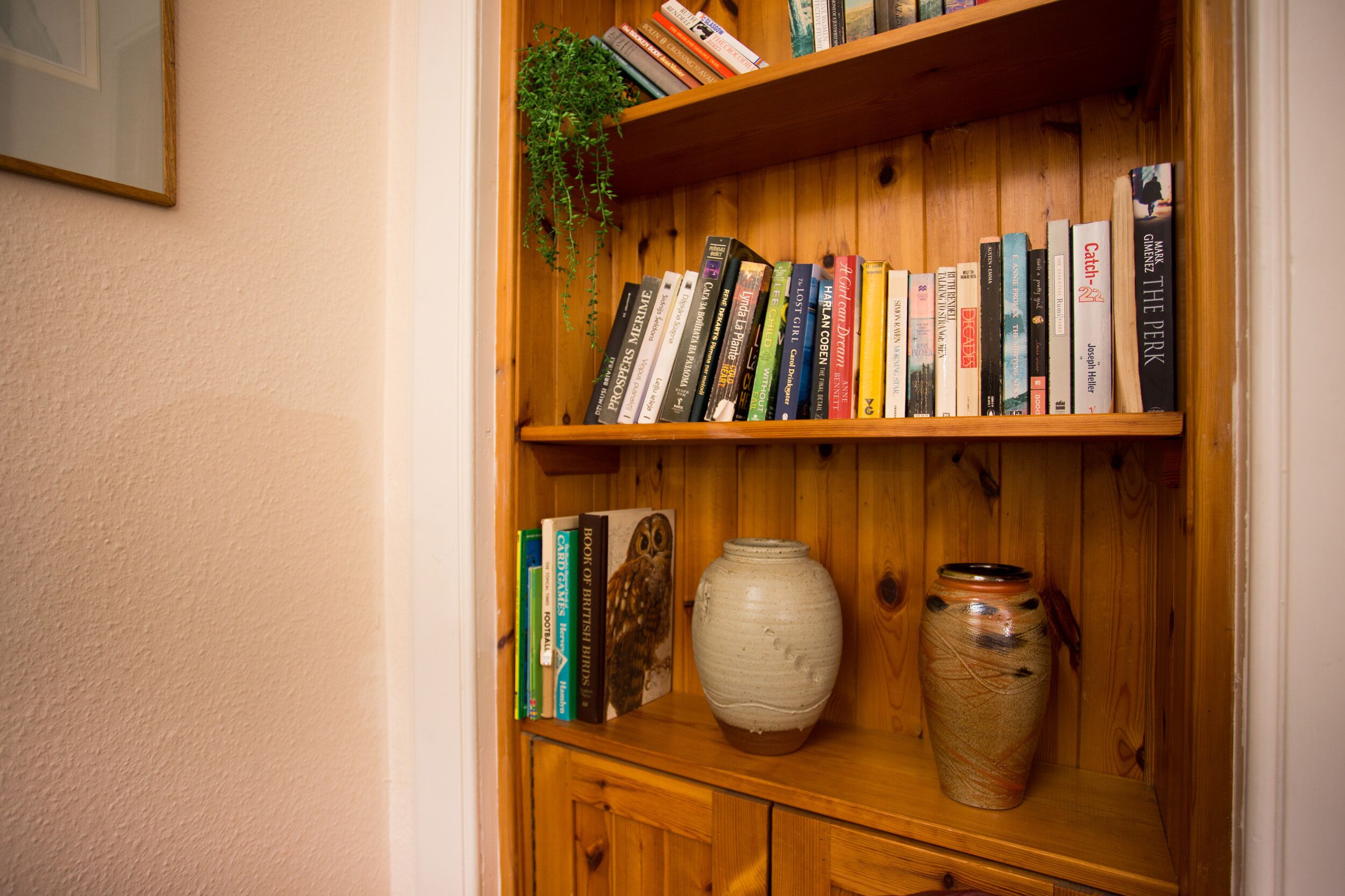 A wooden bookshelf with books and a ceramic vase.