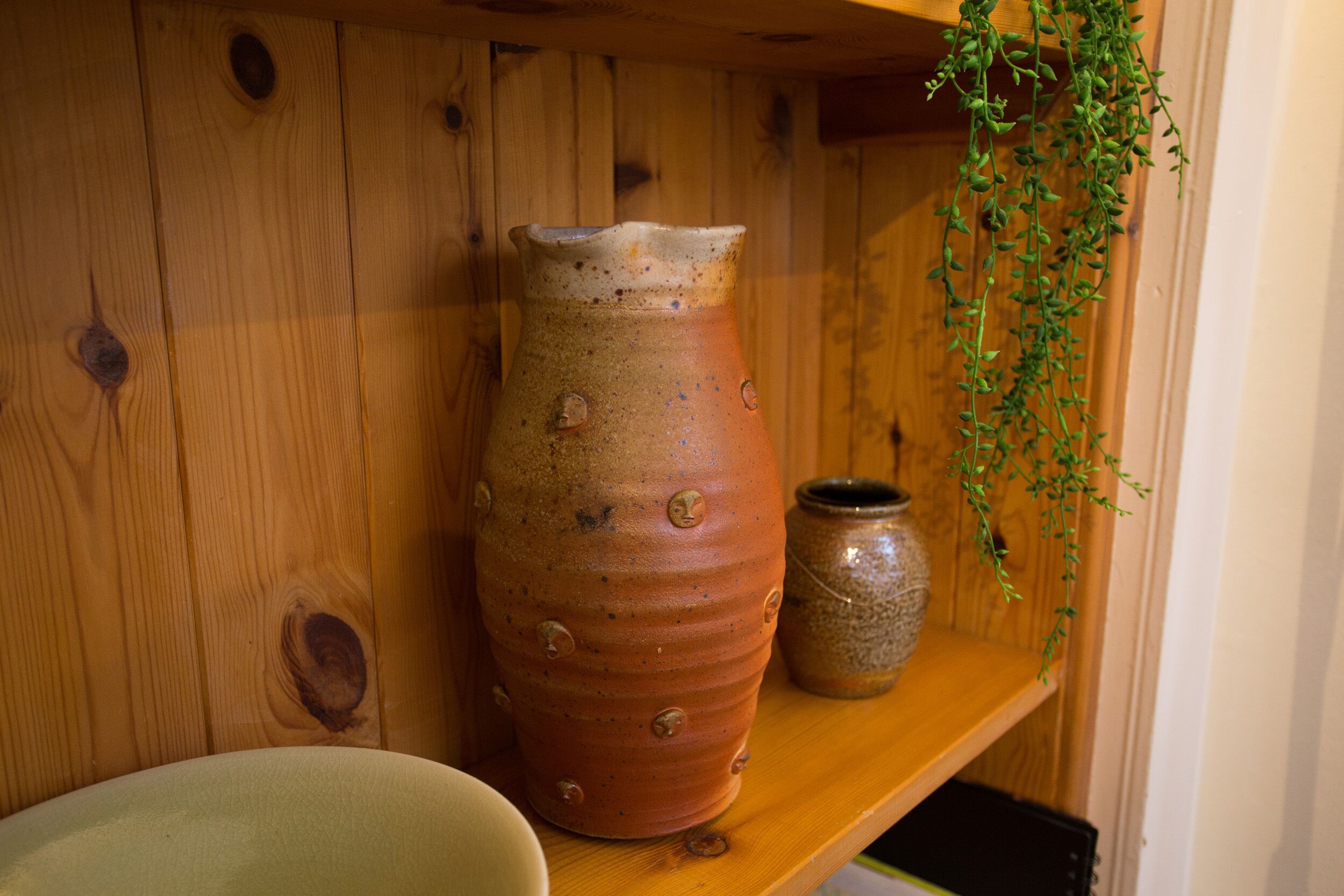 A wooden shelf with two ceramic pots and a hanging plant.