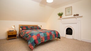 Un dormitorio con cama, mesita de noche, lámpara, chimenea y un cuadro en la pared.