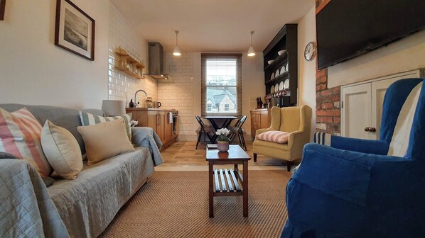 A living room with a sofa, armchairs, a coffee table, and a kitchen in the background.