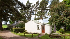 A small white building with a red door, surrounded by a gravel path and wooden fence.